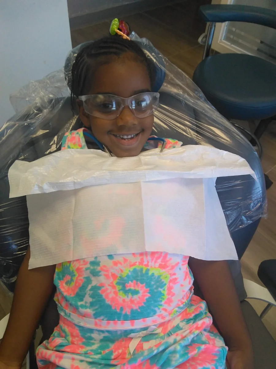 A young patient smiling in the dental chair while wearing protective glasses