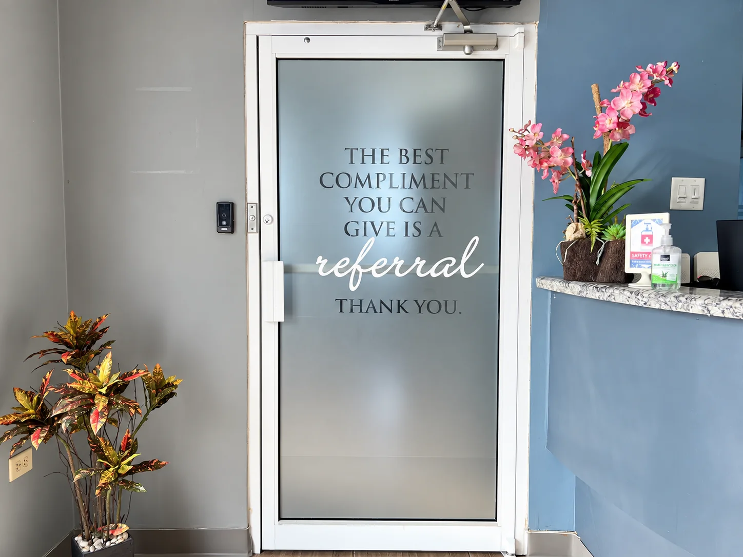 The frosted glass door at Elite Smiles with its referral thank-you message and pink orchids